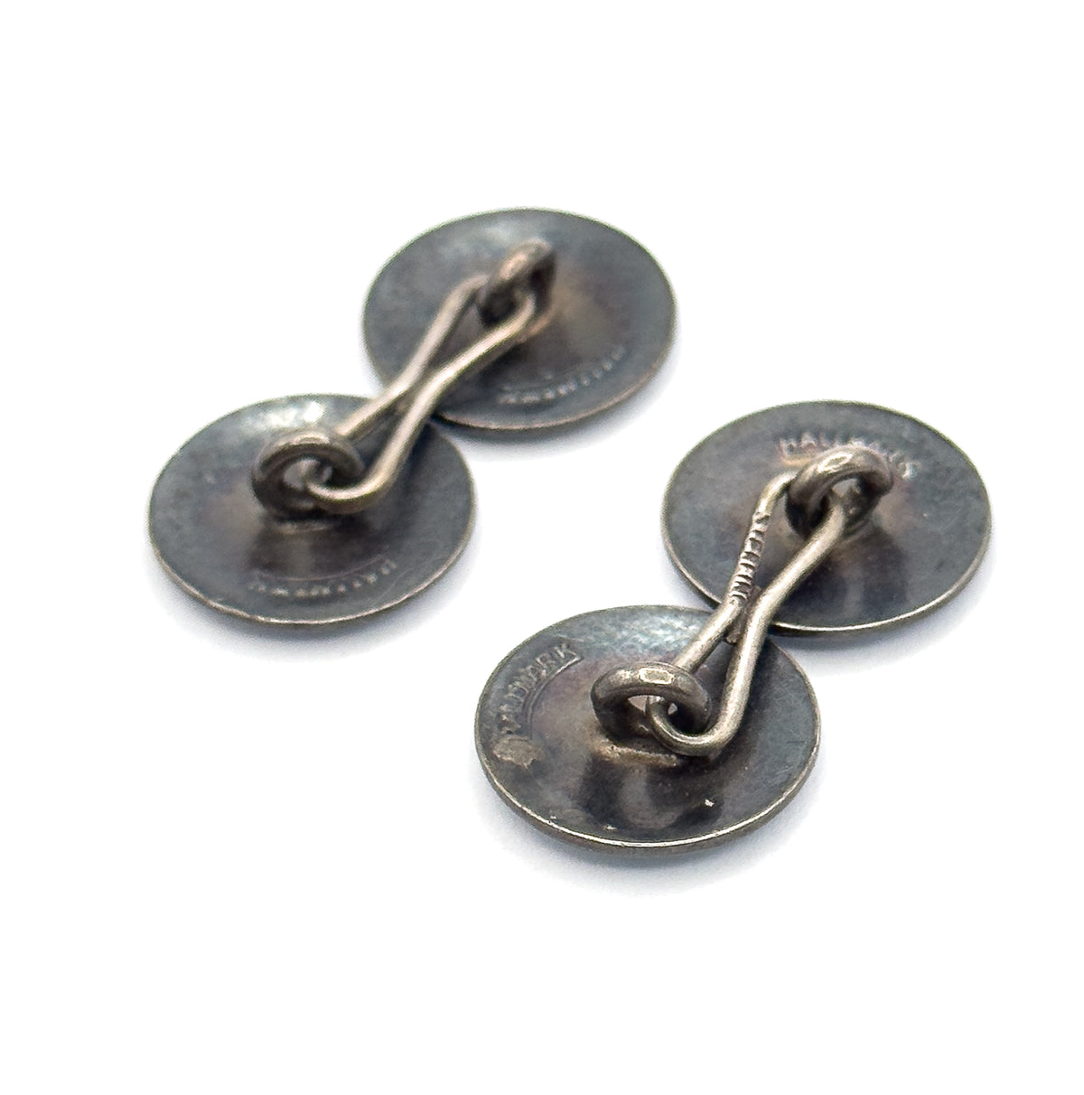 The reverse sides face up, showing the darkened patina on both pairs of discs and the curved toggle bars linking them, with small stamped marks near the rims.