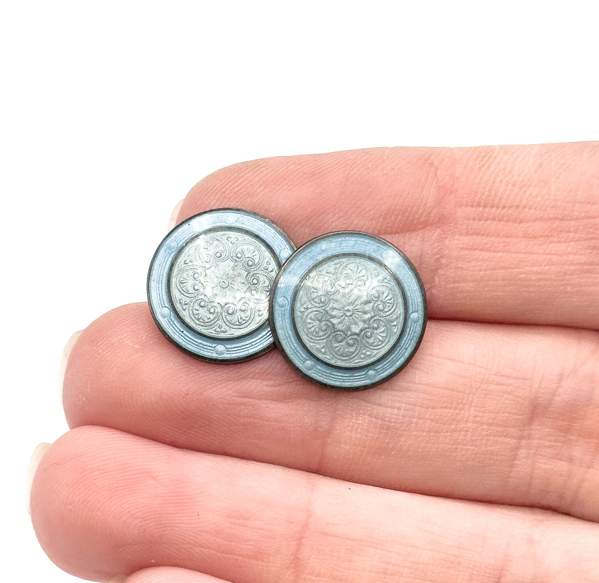 Vintage guilloche enamel cufflinks in sterling silver, the two round discs resting on fingertips to show their small size, each face swirled with grayish and dusty blue enamel.