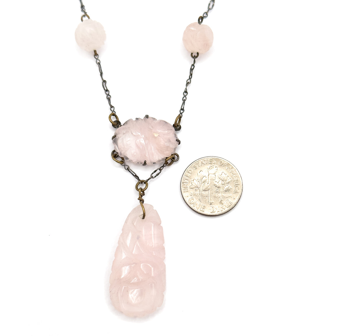 A dime laid beside the lower half for scale, the pronged oval centre station reading about the width of the coin and the long carved rose quartz drop roughly twice its length.