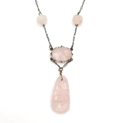 Straight-on symmetrical view of the necklace front on white, both round carved rose quartz beads balanced either side of the pronged oval centre station with the long carved drop hanging centred below.