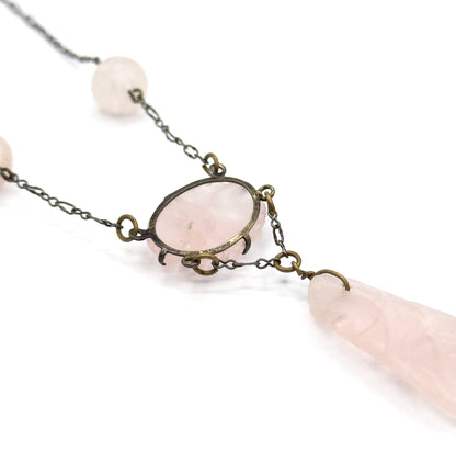 Close view of the oval rose quartz centrepiece held in a pronged setting, with round carved beads along the darkened chain above and the elongated drop stone hanging below.