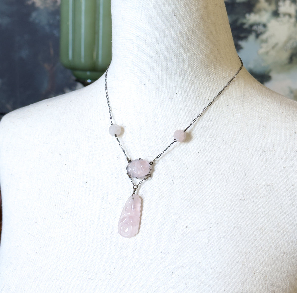 Shown at the neck on a pale linen dress form, the darkened chain draping with its round carved beads to the pronged oval centre and the long carved drop below.