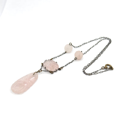 The whole necklace laid out flat at an angle on white, the chain looping away to the clasp at right while the two round carved beads, pronged oval centre and long carved drop trail to the left.