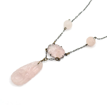 Diagonal view running from the chain at upper right down past both round carved rose quartz beads to the pronged oval centre station and the long carved drop at lower left.