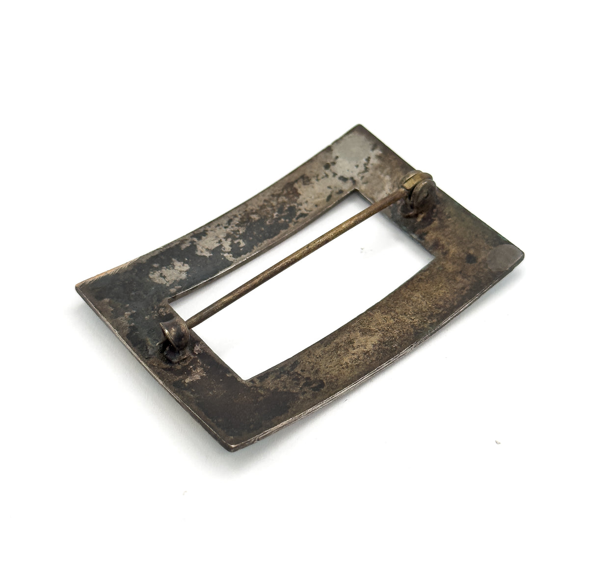 The back of the brooch tilted at an angle on a plain background, showing the hollow rectangular opening with the pin stem running from hinge to catch across it.