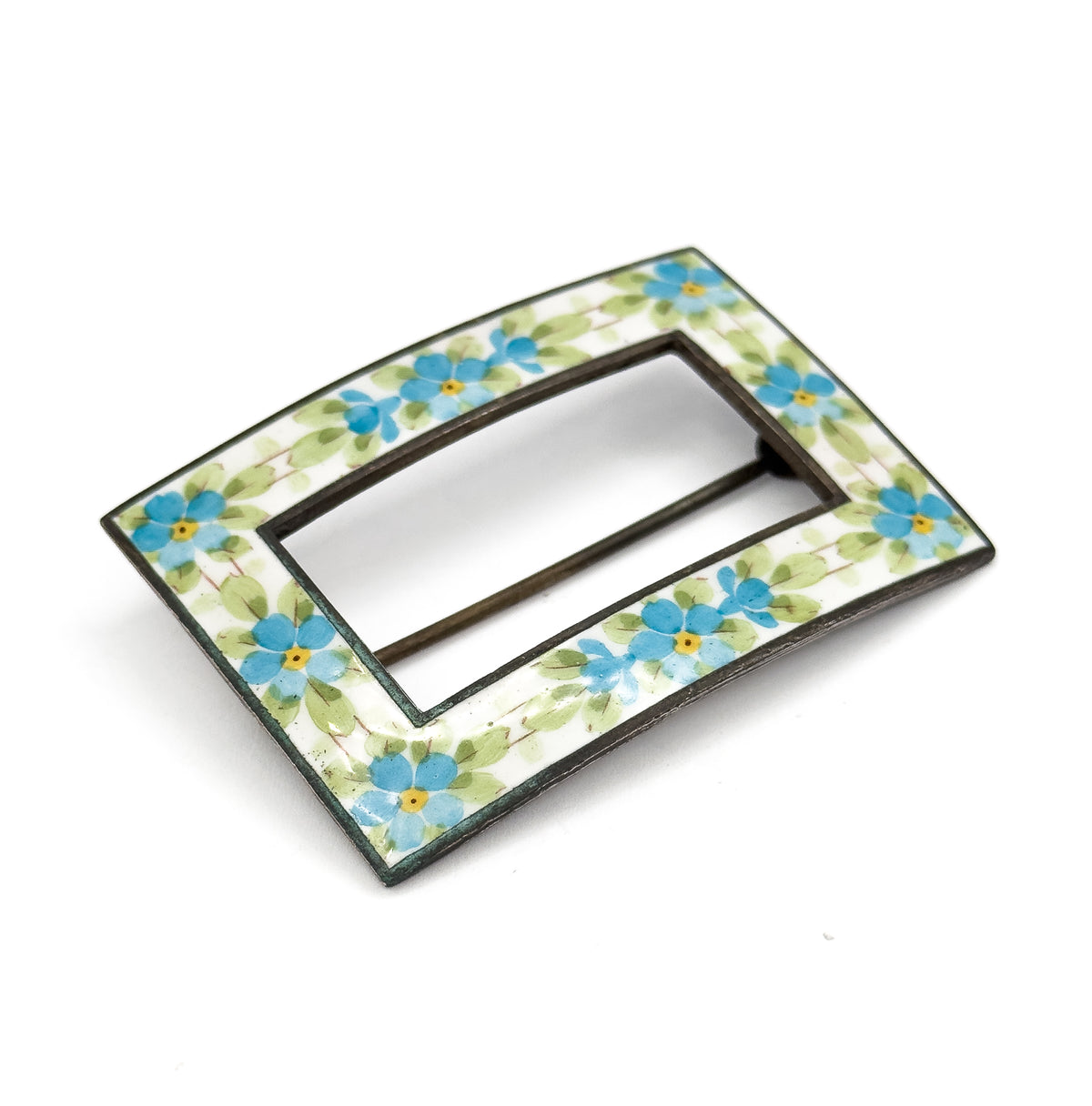 Tilted so the near long edge comes forward, the flower-painted enamel band sweeps around the open centre while the pin stem lies as a thin dark line across the opening behind.