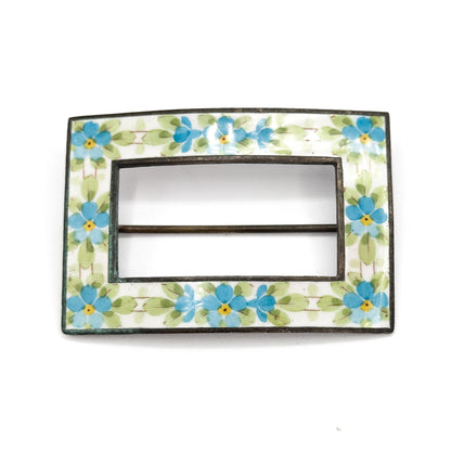 Straight-on front view with no scale object, the rectangular enamel band of blue and yellow flowers filling the frame and the pin stem crossing the open centre as a slim bar.