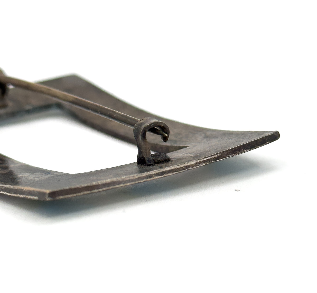 A rectangular enamel brooch in silver plated base metal, shown from the back in close-up with the pin stem crossing the frame and resting in its hook-shaped catch.