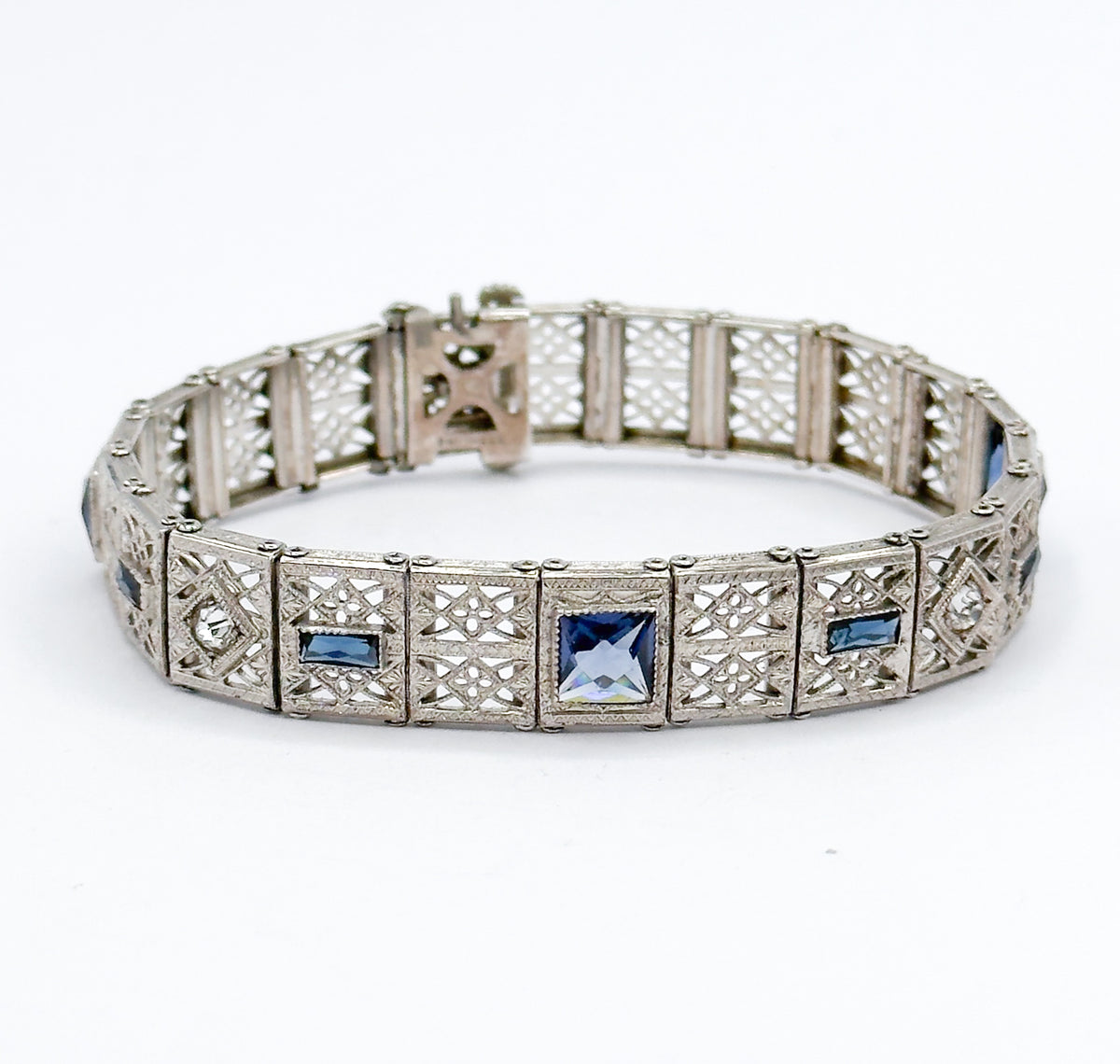 Seen at eye level with the bracelet standing on edge in a ring, the near front links face the camera so a large square blue paste stone sits centred between two blue rectangles.