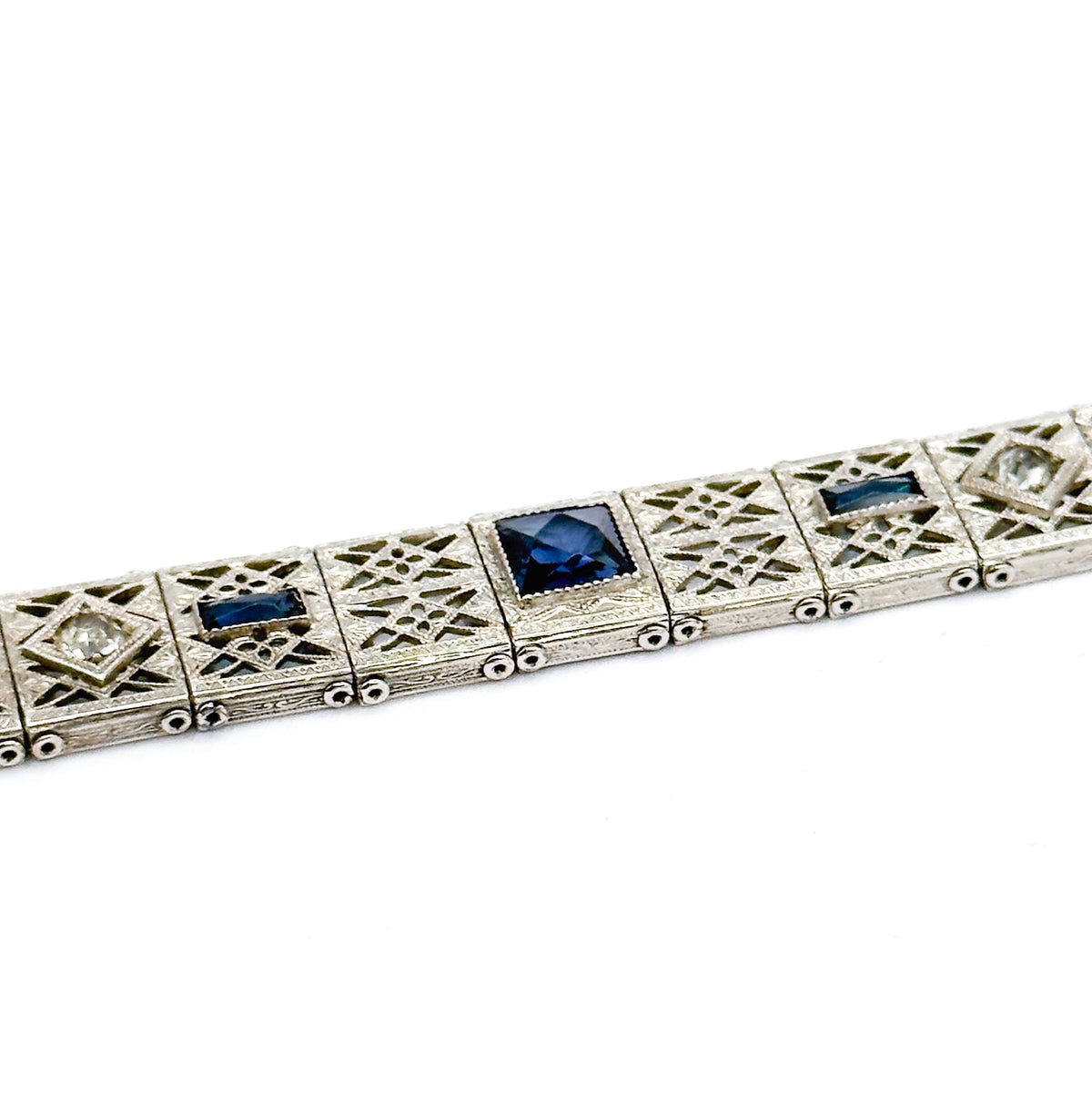 A closer angled view along the link row, showing deep blue paste squares and rectangles in milgrained bezels between openwork filigree panels and their hinged connecting pins.