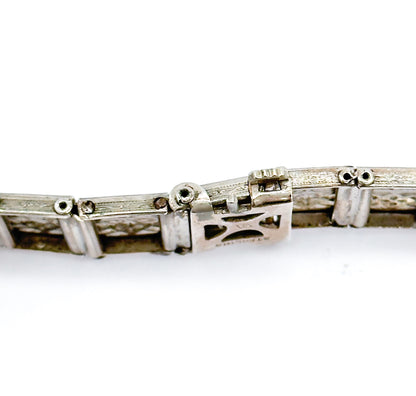 The reverse of the bracelet, where the openwork clasp box carries a small stamped mark beside the pierced backs of the filigree links and their side hinge pins.