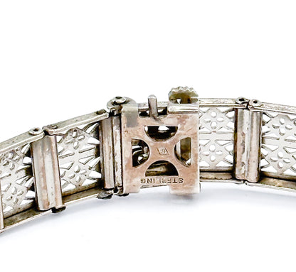 A tight macro of the clasp box underside, where the word STERLING reads upside down beside a tiny square maker's mark, framed by the pierced reverse of the filigree links.