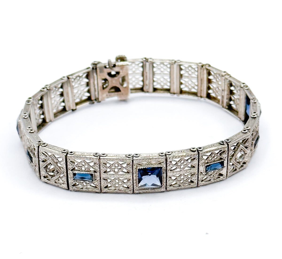 The whole bracelet standing in an open oval, seen from above, so the full circuit of filigree links reads at once with blue paste squares and rectangles spaced around the front.