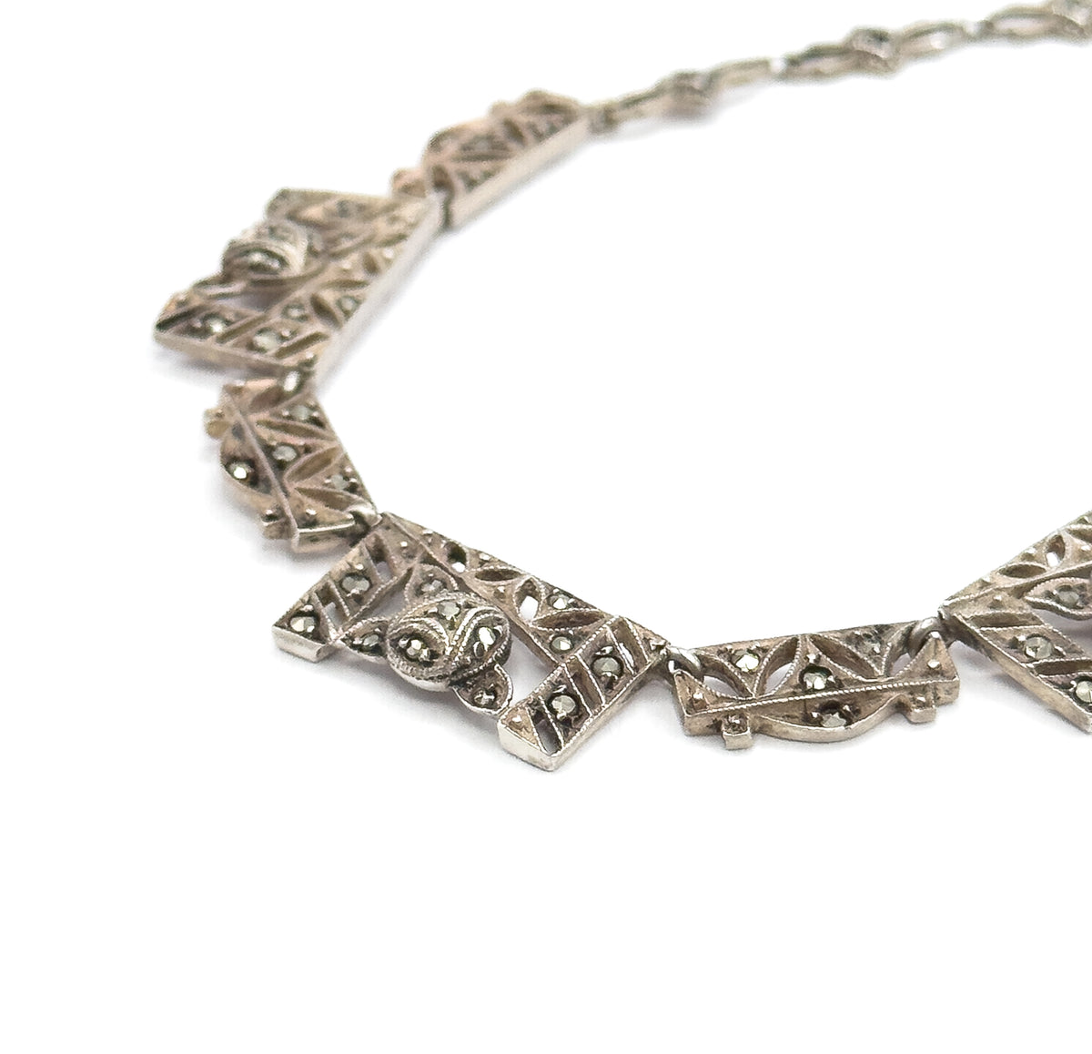 Close view of the front, where chevron-shaped filigree panels set with grey marcasites and a domed central motif curve away into the smaller links at the back.