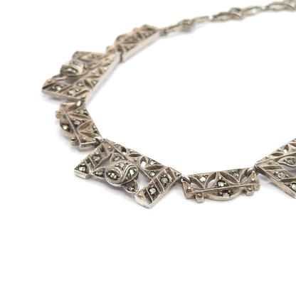 Close view of the front, where chevron-shaped filigree panels set with grey marcasites and a domed central motif curve away into the smaller links at the back.