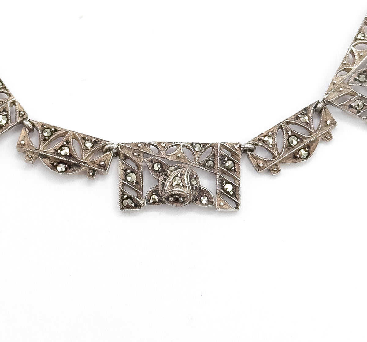 Tight crop on the central rectangular panel, its domed marcasite-set motif and pierced leaf openwork sharply visible between two chevron panels, with milgrain edging along every border.