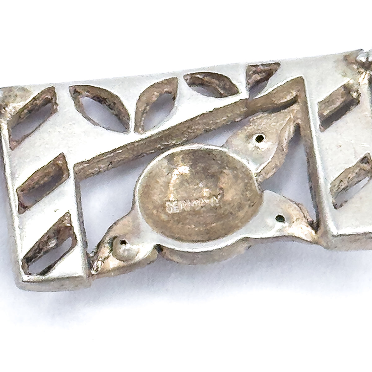 Reverse side in macro, showing the pierced openwork back of one panel with leaf- and bar-shaped cut-outs and a smooth oval plaque carrying a stamped word.