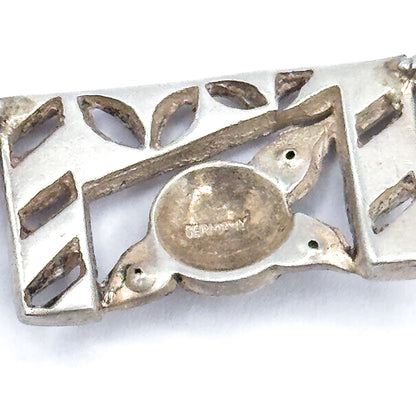Reverse side in macro, showing the pierced openwork back of one panel with leaf- and bar-shaped cut-outs and a smooth oval plaque carrying a stamped word.