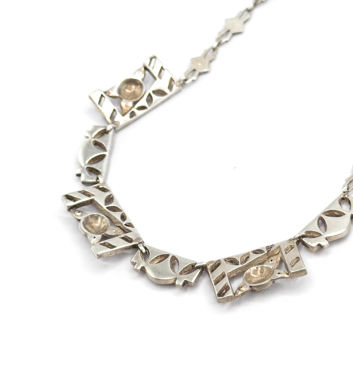 Reverse view along the curve of the necklace, showing several panels' pierced undersides with their smooth oval plaques and the open star-shaped chain links trailing away.