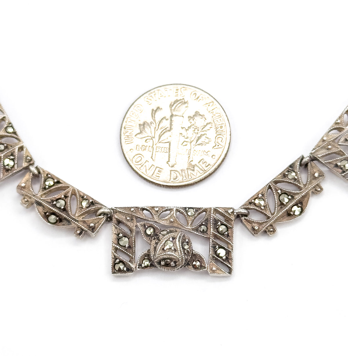A dime rests above the central panels for scale, each filigree link set with grey marcasites measuring well under the coin's width.
