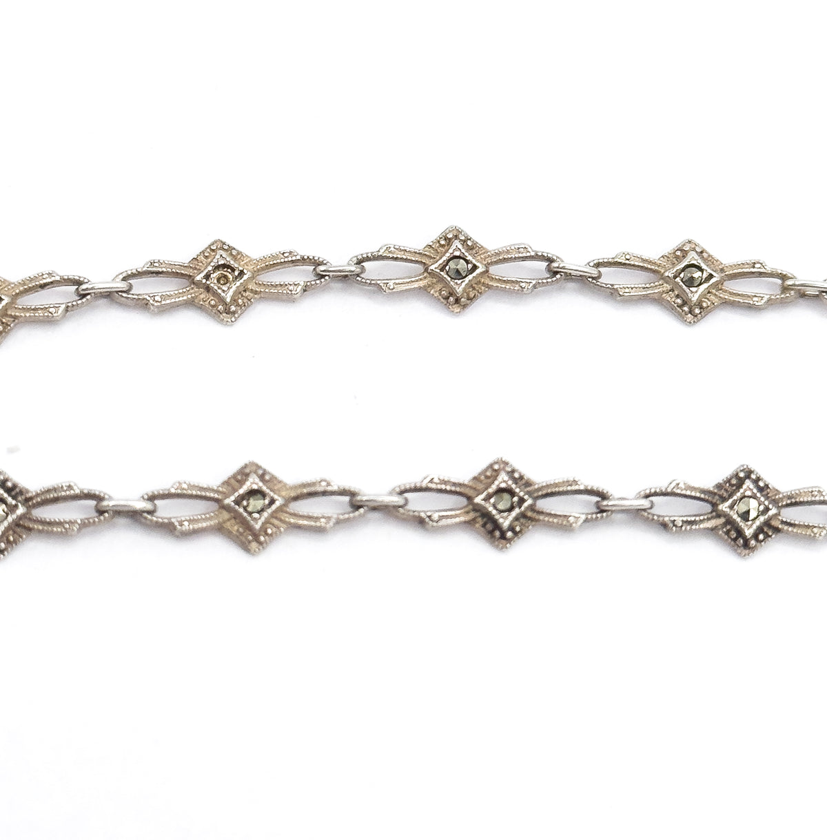 Two parallel lengths of the chain in close macro, each lozenge-shaped link centred with a single grey marcasite in a milgrain border and joined by elongated openwork connectors.