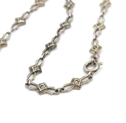 The spring ring clasp at the end of the chain, its sprung lever visible beside the lozenge-shaped marcasite links that curve away across the white background.