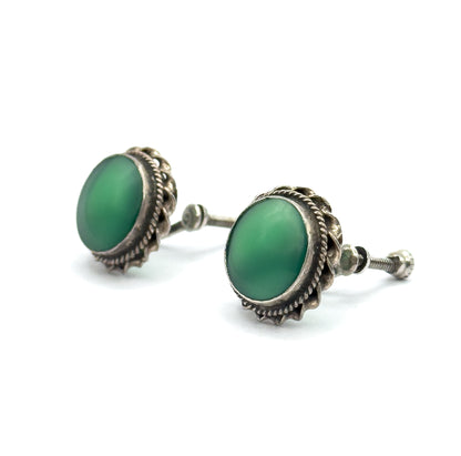 A low side view showing the green cabochons in profile within their bezels, with one screw-back threaded post extending clearly to the right.