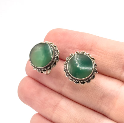 Both earrings resting on fingertips, the green cabochons and cable-edged bezels giving a clear sense of scale against the fingers.