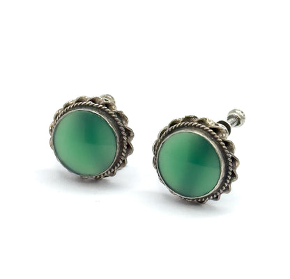 Angled front view of the pair side by side, both round chrysoprase cabochons facing the camera within scalloped cable-textured sterling silver bezels, one knurled screw head peeking at the right.