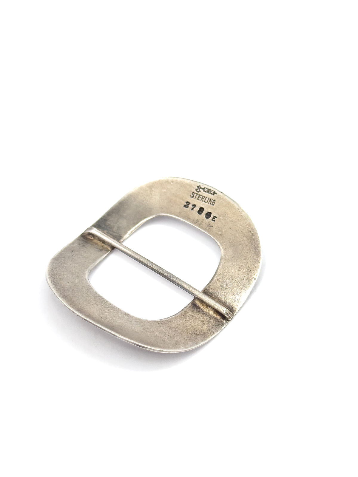 Almost the same view with slightly different angle, the buckle rotated so the stamped marks read upright and the rounded outer edge shows its slim depth against white.