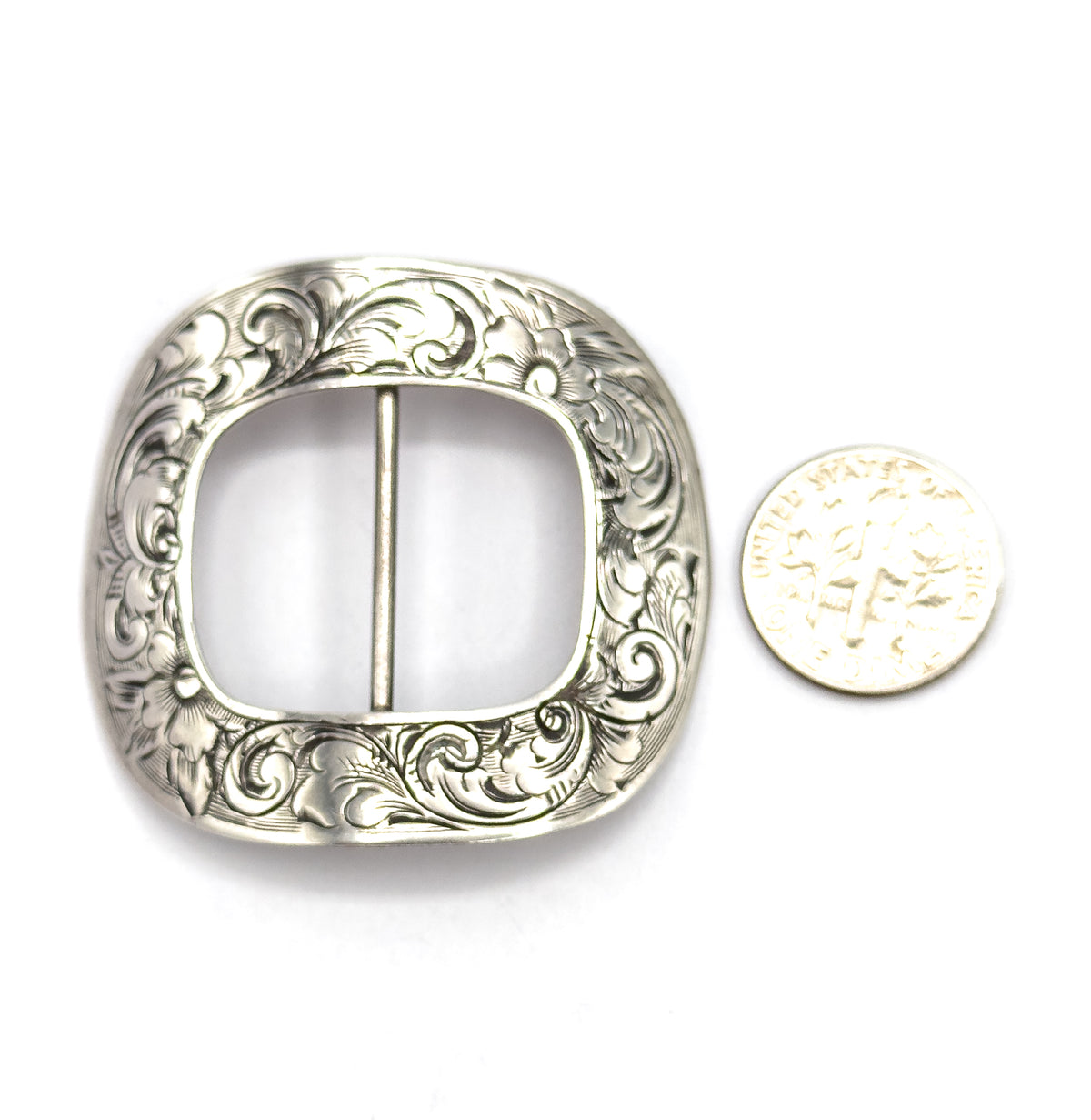 The engraved face flat on white beside a dime for scale, the buckle standing roughly four times the coin's width with its floral scrollwork framing the open centre bar.