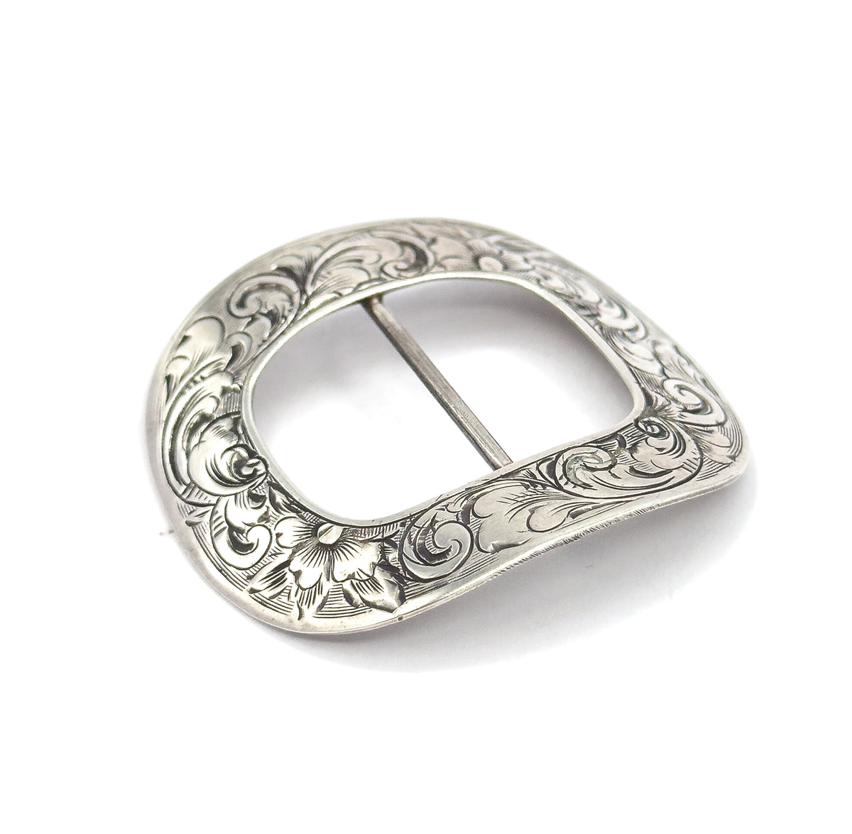 The engraved face tilted toward the viewer on white, light raking across the raised scrollwork and a single open flower at the lower edge while the central bar crosses the oval opening.