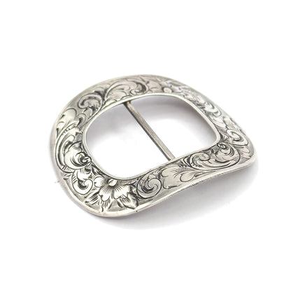 The engraved face tilted toward the viewer on white, light raking across the raised scrollwork and a single open flower at the lower edge while the central bar crosses the oval opening.