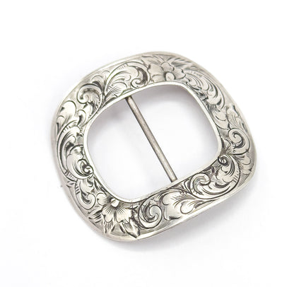 The engraved face seen straight on with the central bar running vertically, showing the squared-oval outline and a hand engraved flower at both the top and bottom of the scrolling border.