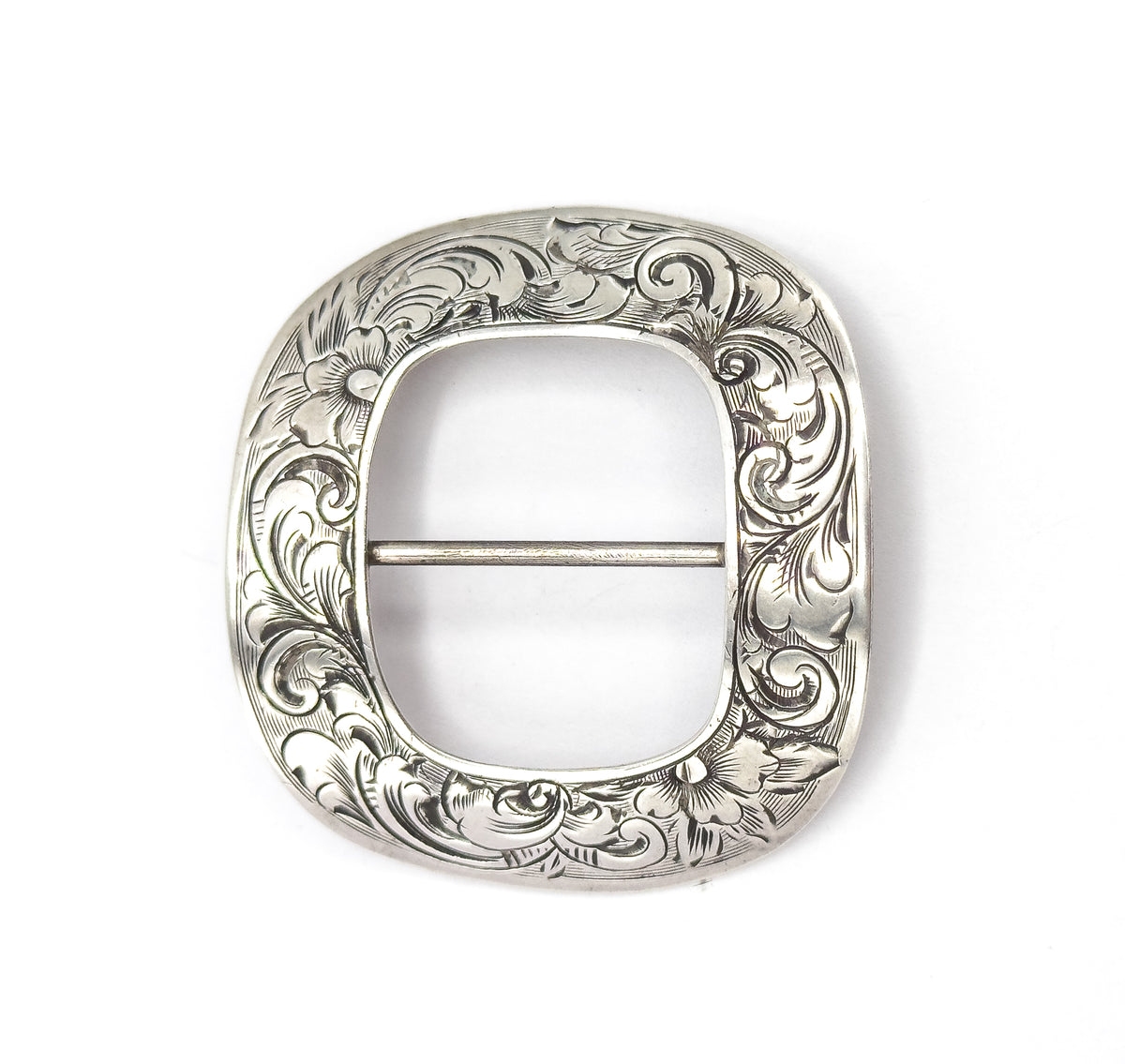 The sterling silver buckle laid flat and square to the camera with the central bar running horizontally across the open centre, engraved scrolls and flowers filling the full width of the frame.