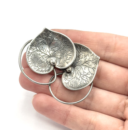 Shown face up on an open palm, the two etched sterling silver hearts with their small central beads span about two fingers' width, the looping connector curving below.