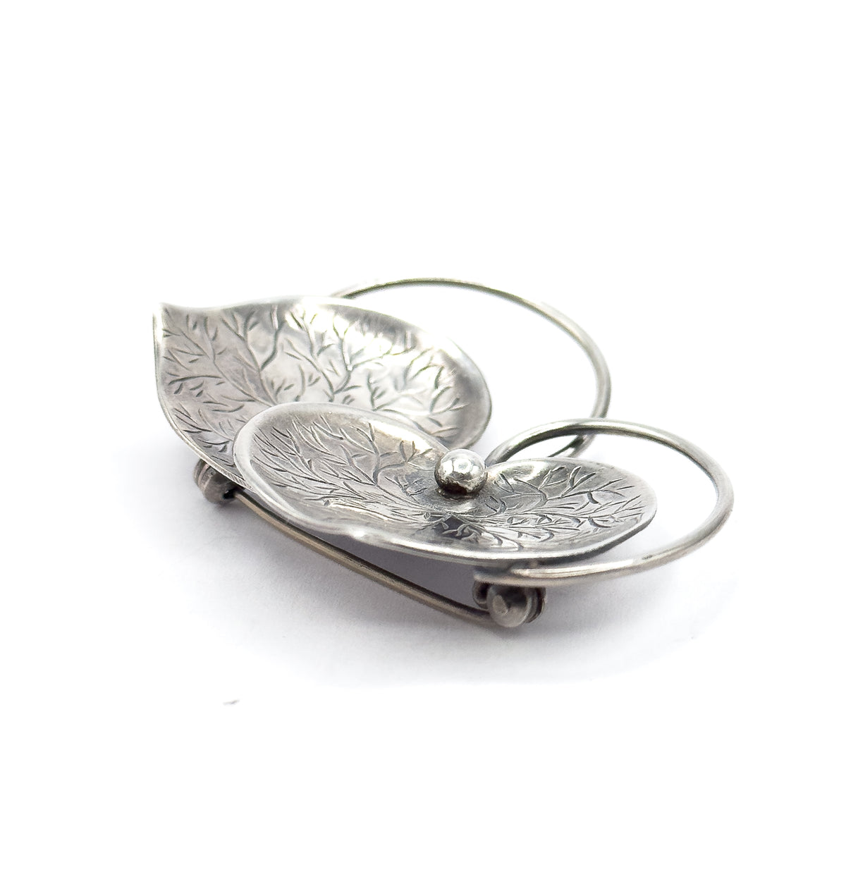 Low angled side view on white, showing how the two etched hearts dish upward from the looping wire connector, with a small raised bead at the centre and the pin stem visible behind.