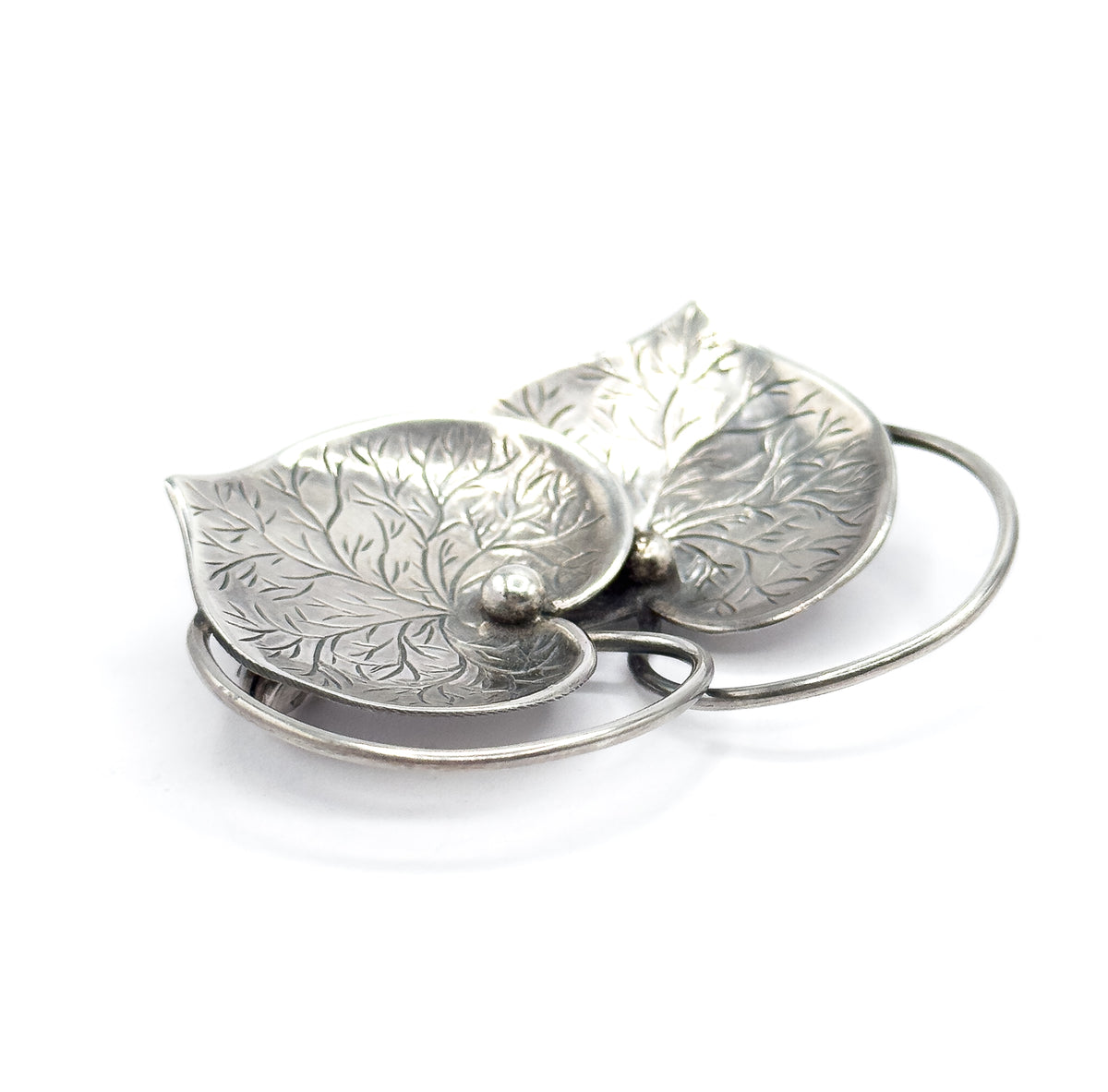 Tilted close view from the tip of one heart, the fine etched veining filling both sterling silver hearts while the looping wire connector crosses in open curves beneath them.