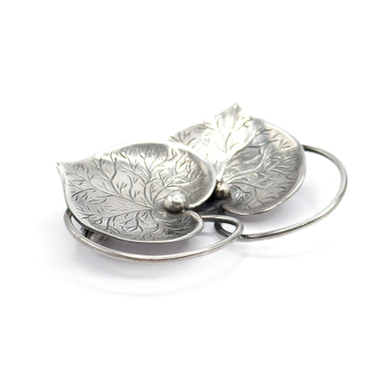 Tilted close view from the tip of one heart, the fine etched veining filling both sterling silver hearts while the looping wire connector crosses in open curves beneath them.
