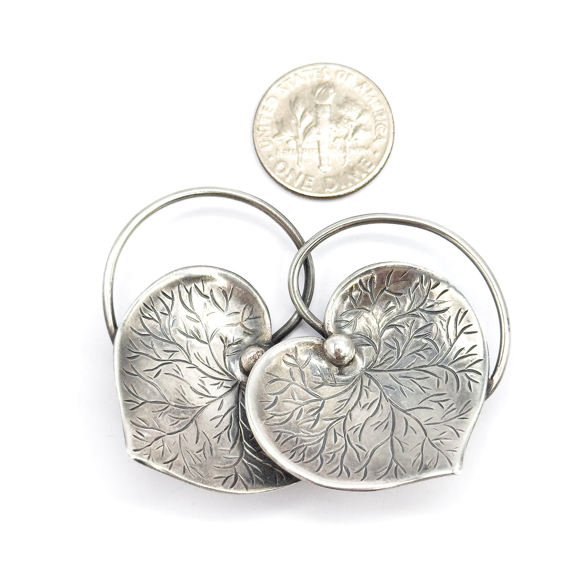 Shown beside a dime for scale, the paired etched hearts together measure roughly twice the coin's width, with the looping wire connector arching behind them.