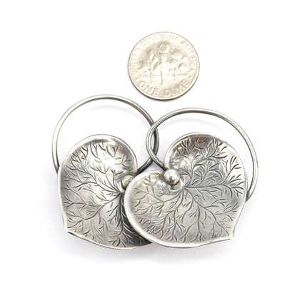 Shown beside a dime for scale, the paired etched hearts together measure roughly twice the coin's width, with the looping wire connector arching behind them.