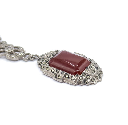 Close three-quarter view from the side, the rectangular carnelian rising in a stepped cabochon above its scalloped marcasite-set frame, with one chain station behind.
