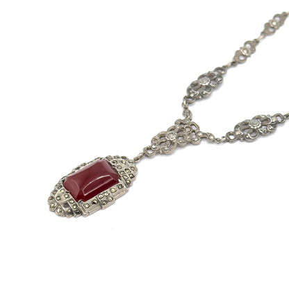 Diagonal overhead view with the carnelian pendant at lower left and the chain sweeping to the upper right, its floral openwork marcasite stations linked in a receding line.