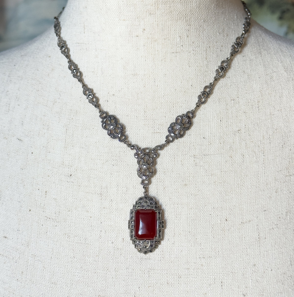 Displayed on a linen neck form, the necklace drapes in a V with marcasite-set openwork stations meeting a triangular link that suspends the rectangular carnelian pendant.