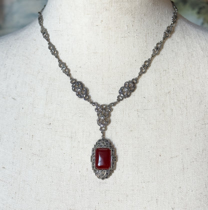 Displayed on a linen neck form, the necklace drapes in a V with marcasite-set openwork stations meeting a triangular link that suspends the rectangular carnelian pendant.