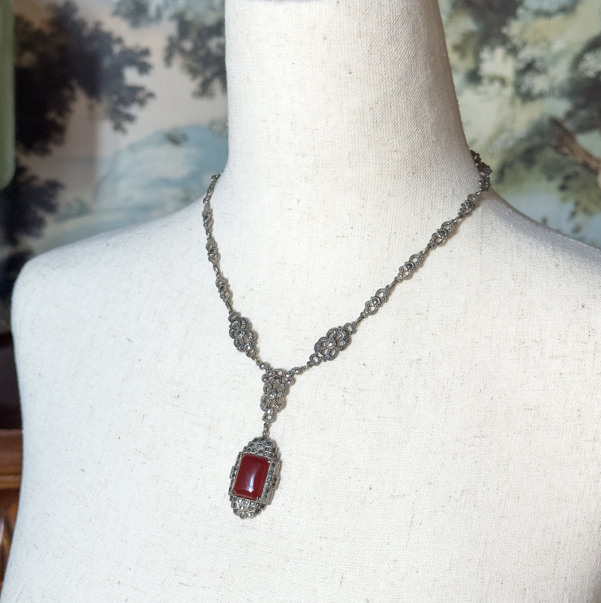 Almost the same view with slightly different angle, the neck form turned so the chain stations catch the light and the carnelian pendant hangs centred against the linen.