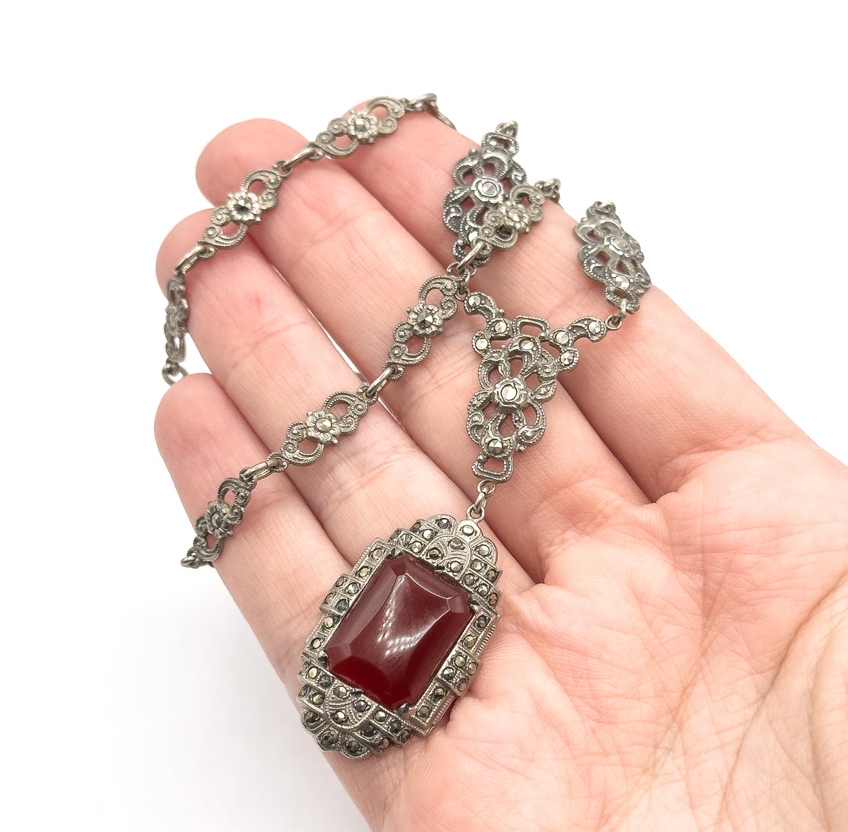 Draped across an open palm for scale, the rectangular carnelian pendant in its marcasite-set frame rests on the fingers with the openwork chain stations coiled above.