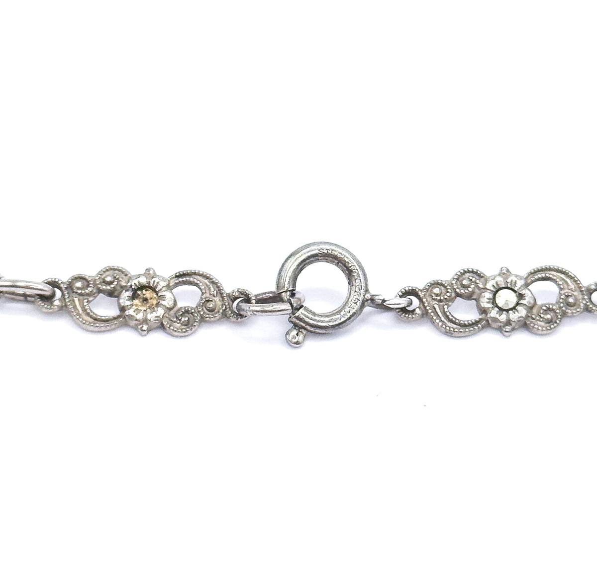 Close-up on the round spring-ring clasp, flanked by two scrolled openwork chain stations with marcasite-set flower centres and small jump rings linking them.