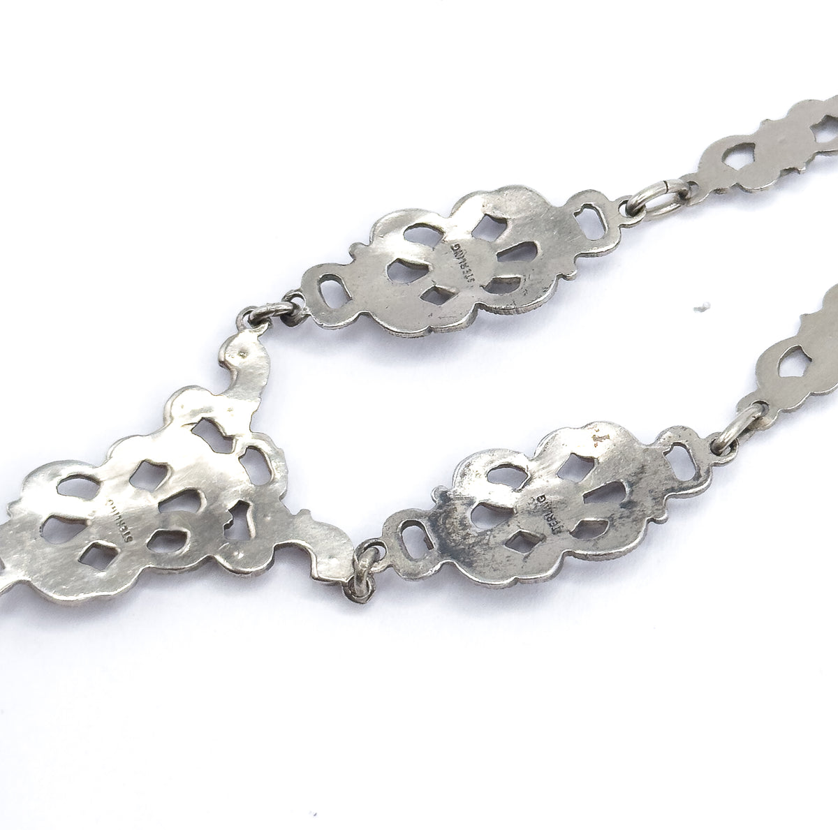 Reverse of the chain, showing the flat backs of the scrolled stations with their open cut-out centres and STERLING stamps, joined by oval links and jump rings.
