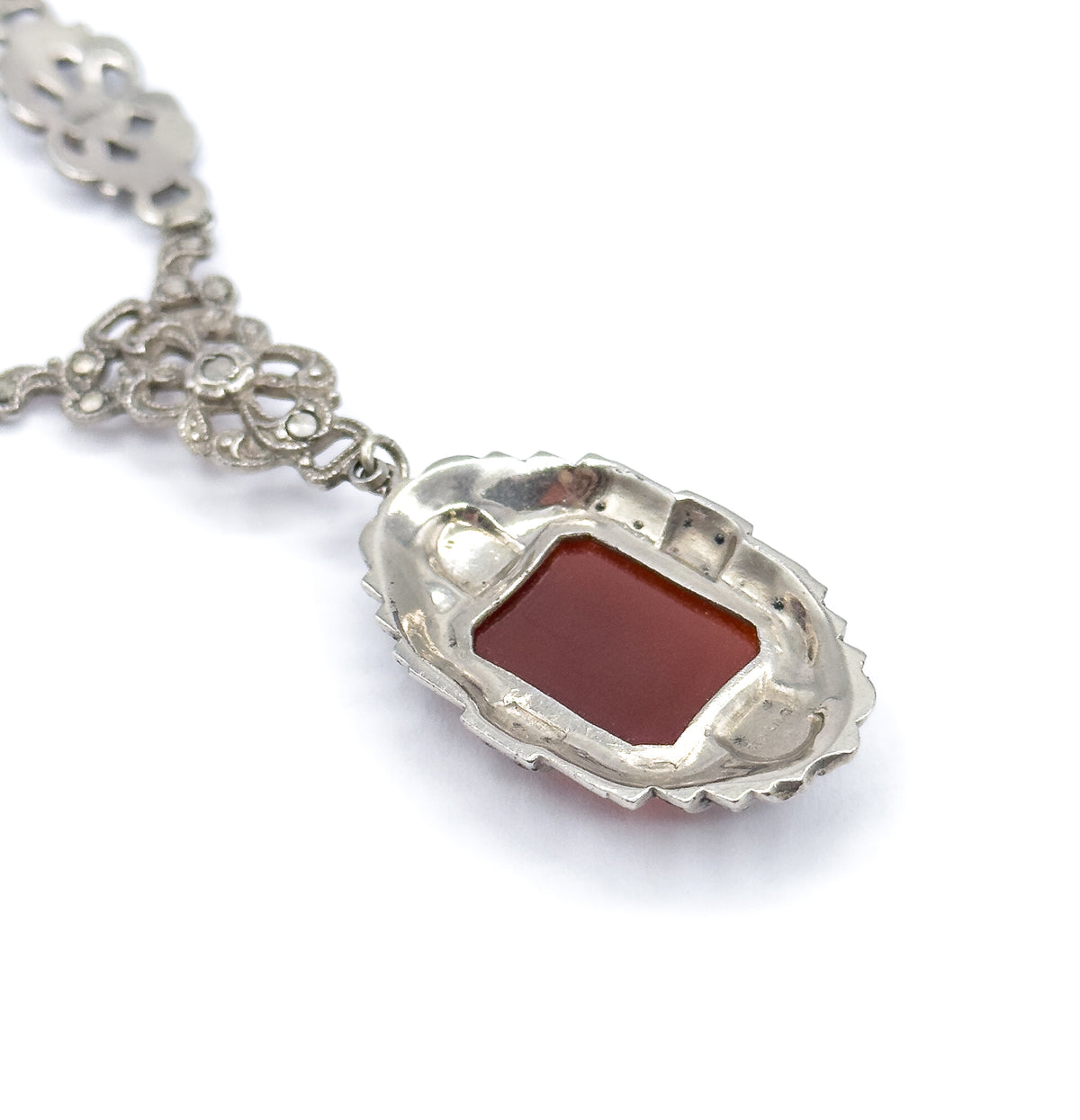 Angled view of the pendant's reverse, where the carnelian shows through the open back of its scalloped sterling silver frame, with two chain stations and the bail link receding behind.